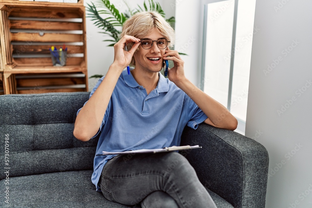 Poster Young blond man psychologist reading document talking on smartphone at psychology clinic