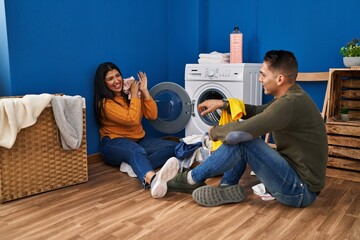 Man and woman couple smiling confident playing with clothes at laundry room