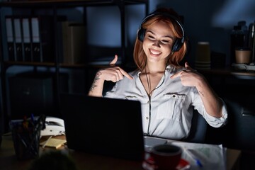 Young caucasian woman working at the office at night looking confident with smile on face, pointing oneself with fingers proud and happy.