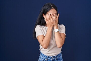 Young hispanic woman standing over blue background with sad expression covering face with hands while crying. depression concept.