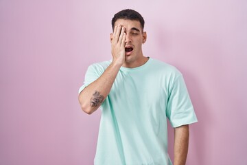 Handsome hispanic man standing over pink background yawning tired covering half face, eye and mouth with hand. face hurts in pain.