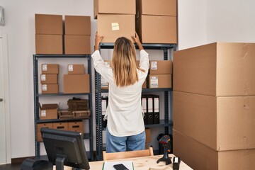 Young hispanic woman ecommerce business worker organizing pacakges on shelving at office