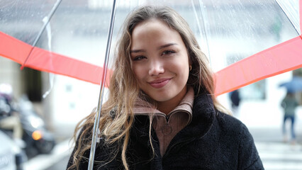 Young beautiful hispanic woman smiling confident holding umbrella at street