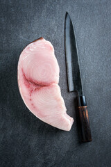Raw and fresh sword fish steak offered with a Japanese Gyuto knife as top view on a gray design...