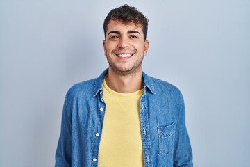 Young hispanic man standing over blue background with a happy and cool smile on face. lucky person.