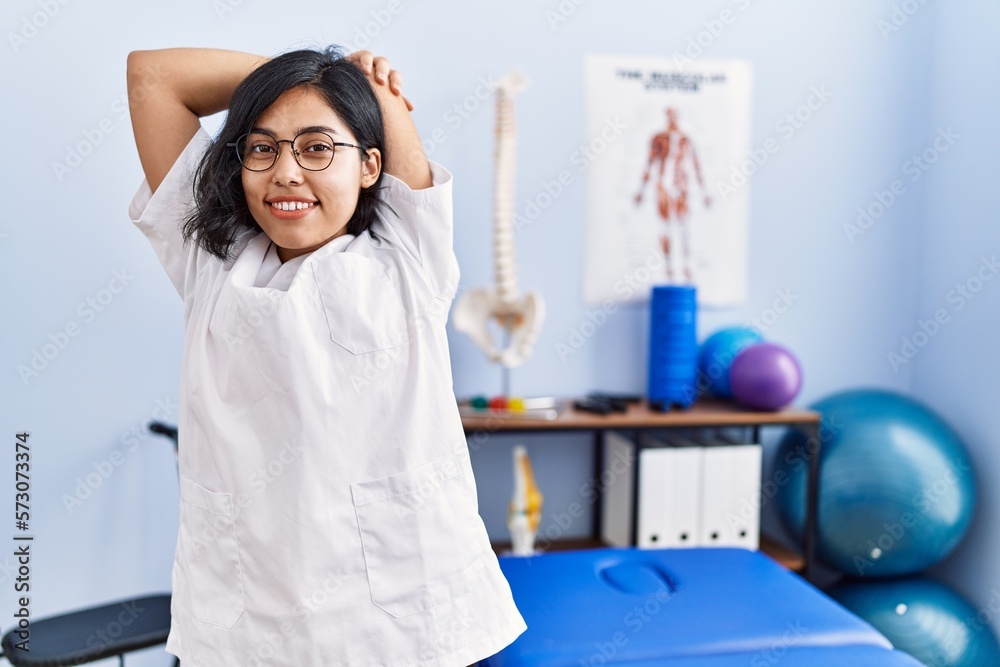 Poster young latin woman wearing doctor uniform stretching arms at physiotherapy clinic