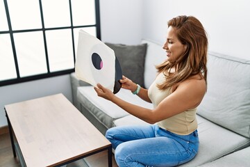 Young latin woman smiling confident holding vinyl disc at home