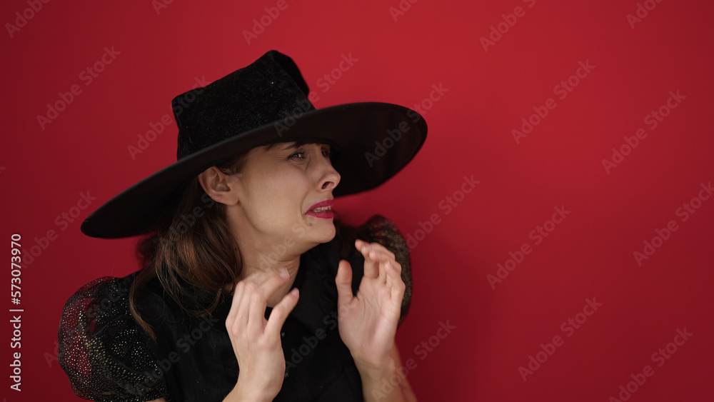 Sticker Young caucasian woman looking afraid wearing witch costume over isolated red background