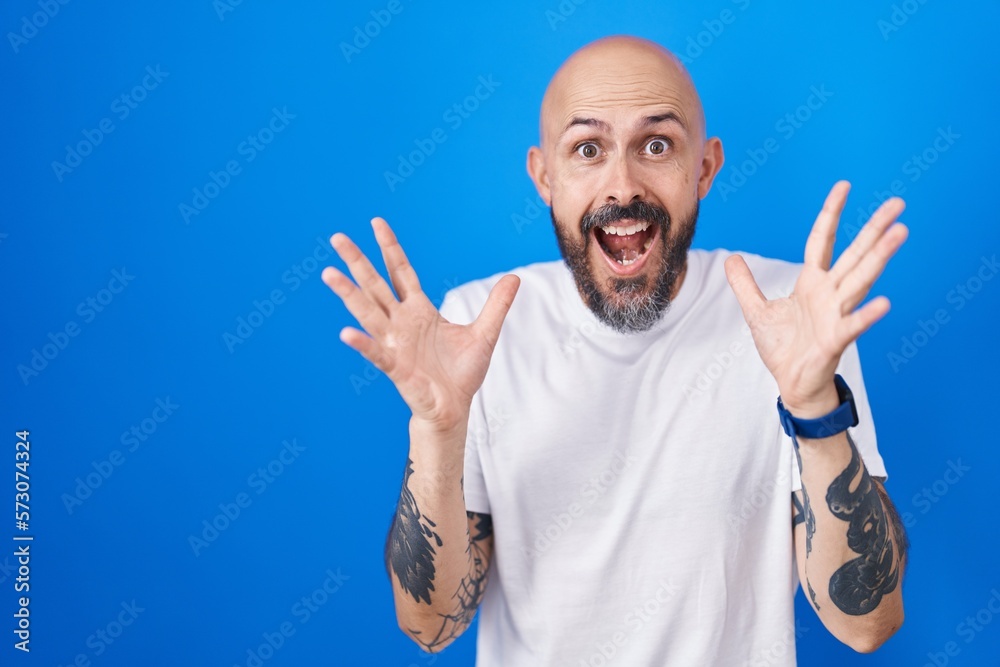 Sticker Hispanic man with tattoos standing over blue background celebrating crazy and amazed for success with arms raised and open eyes screaming excited. winner concept