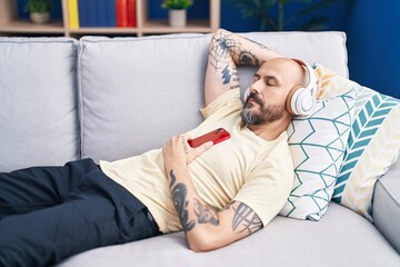 Young bald man listening to music sleeping on sofa at home