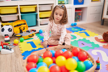 Adorable hispanic girl playing with balls sitting on floor at kindergarten