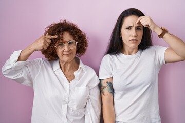 Hispanic mother and daughter wearing casual white t shirt over pink background pointing unhappy to...