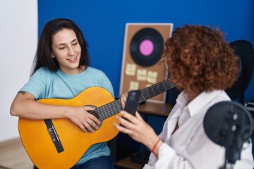 Two women musicians having classical guitar lesson by smartphone video at music studio