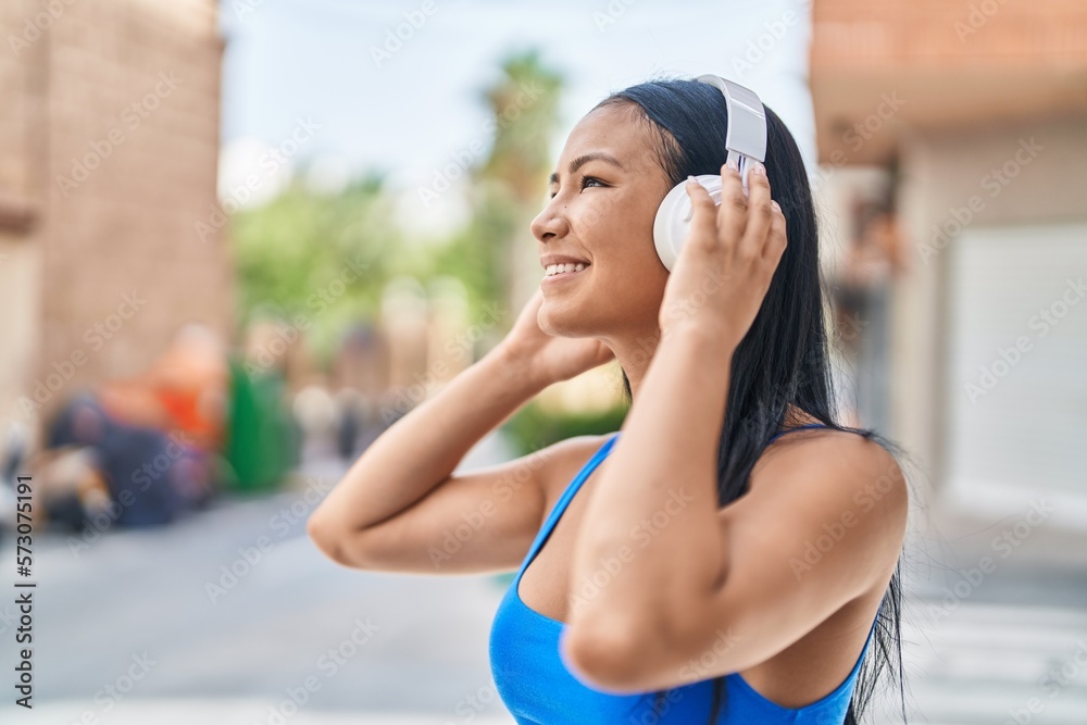 Wall mural Young beautiful latin woman listening to music and at street