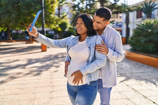 Young latin couple expecting baby making selfie by the touchpad at park
