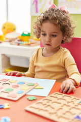 Adorable hispanic toddler playing with maths puzzle game sitting on table at kindergarten