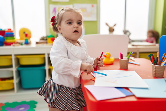Adorable blonde toddler preschool student drawing on paper standing at kindergarten