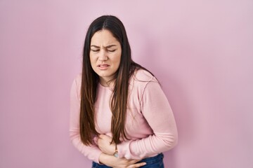 Fototapeta premium Young brunette woman standing over pink background with hand on stomach because indigestion, painful illness feeling unwell. ache concept.