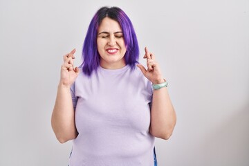 Obraz na płótnie Canvas Plus size woman wit purple hair standing over isolated background gesturing finger crossed smiling with hope and eyes closed. luck and superstitious concept.