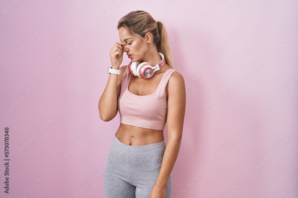 Poster young blonde woman wearing sportswear and headphones tired rubbing nose and eyes feeling fatigue and