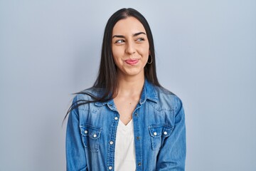 Fototapeta premium Hispanic woman standing over blue background smiling looking to the side and staring away thinking.