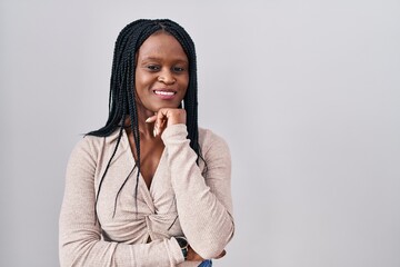 African woman with braids standing over white background with hand on chin thinking about question, pensive expression. smiling and thoughtful face. doubt concept.