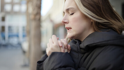 Young blonde woman praying with closed eyes at street