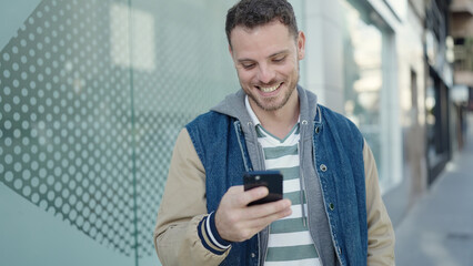 Young caucasian man smiling using smartphone at street