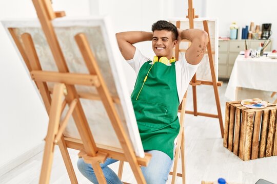 Young hispanic man smiling confident relaxed with hands on head at art studio