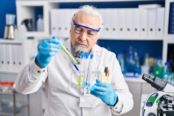 Middle age grey-haired man scientist holding test tubes at laboratory