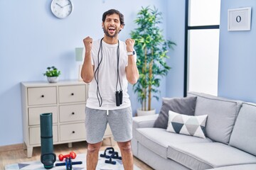 Handsome latin man wearing sportswear at home celebrating mad and crazy for success with arms...