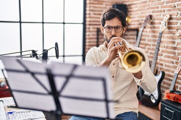 Young hispanic man musician playing trumpet at music studio