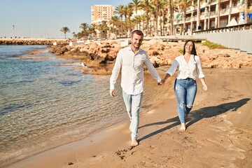 Man and woman couple smiling happy walking at seaside