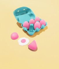 Trendy abstract composition made of pink Easter eggs and a blue box on a pastel yellow...