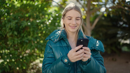Young blonde woman using smartphone at park
