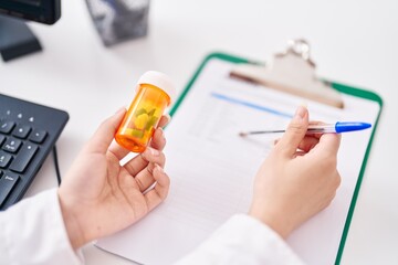 Young chinese woman pharmacist writing on document holding pills bottle at pharmacy