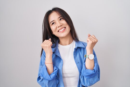 Young chinese woman standing over white background celebrating surprised and amazed for success with arms raised and eyes closed. winner concept.