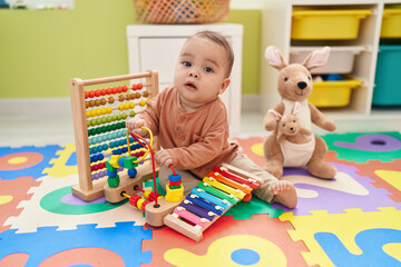 Adorable hispanic toddler playing xylophone sitting on floor at kindergarten