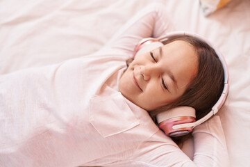 Adorable hispanic girl listening to music lying on bed at bedroom