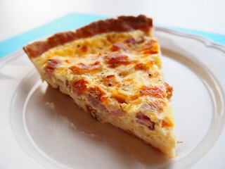 Homemade traditional french Quiche Lorraine, real recipe, slice on a plate, closeup, white and blue background