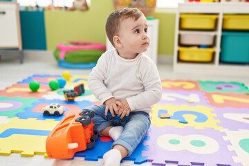 Adorable caucasian baby playing with truck toy sitting on floor at kindergarten