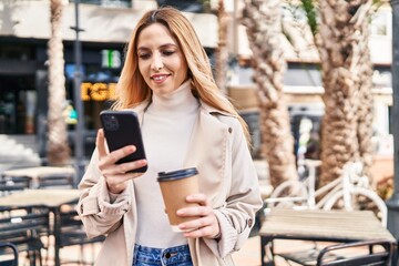 Young blonde woman using smartphone drinking coffee at coffee shop terrace