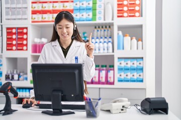 Chinese young woman working at pharmacy drugstore wearing headset smiling with an idea or question pointing finger with happy face, number one