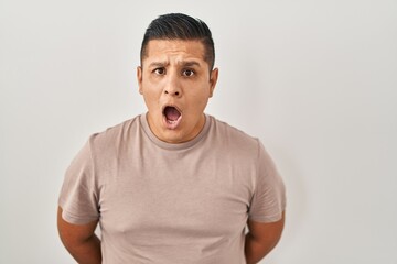 Hispanic young man standing over white background afraid and shocked with surprise expression, fear and excited face.