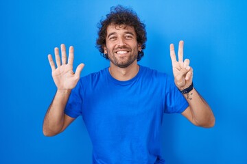 Hispanic young man standing over blue background showing and pointing up with fingers number seven...