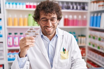 Young hispanic man pharmacist smiling confident holding pills tablet at pharmacy