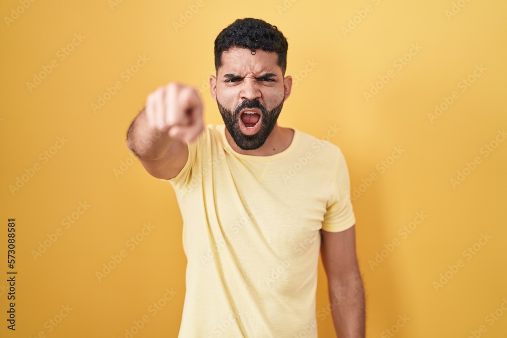 Wall mural Hispanic man with beard standing over yellow background pointing displeased and frustrated to the camera, angry and furious with you