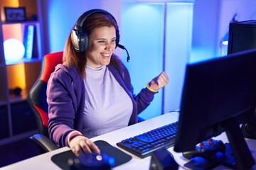 Young beautiful plus size woman streamer playing video game with winner expression at gaming room