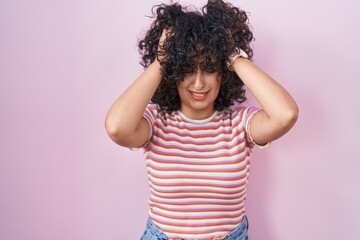 Young middle east woman standing over pink background suffering from headache desperate and stressed because pain and migraine. hands on head.