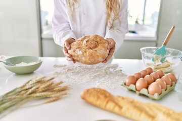 Young woman wearing cook uniform holding bread at kitchen